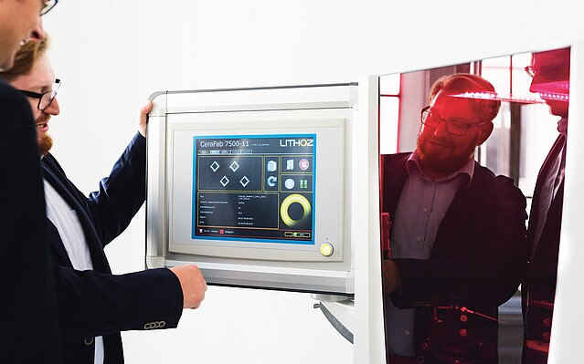 Lithoz: Zwei Männer stehen vor dem Bildschirm eines 3D Druckers.